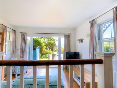 A living room with patterned armchair television and sliding glass door leading to a garden at Little Bay View in Lyme Regis