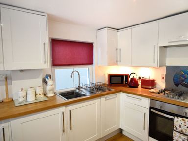 A kitchen with white cabinets a wooden countertop a sink with a dish rack a red microwave kettle and toaster at Little Bay View in Lyme Regis