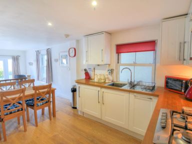 A kitchen with white cabinets wooden countertops dining table with chairs and a red window blind at Little Bay View in Lyme Regis