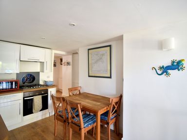 A kitchen with wooden dining table and four chairs next to white cabinets and an oven at Little Bay View in Lyme Regis
