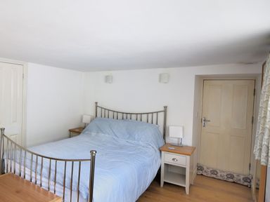 A bedroom with a metal bed frame blue bedding two bedside tables with lamps and a wooden door at Little Bay View in Lyme Regis