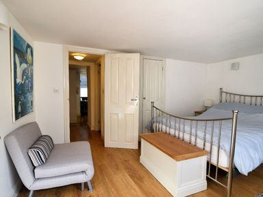 A bedroom with a metal bed frame a light gray chair and a wooden chest at Little Bay View in Lyme Regis