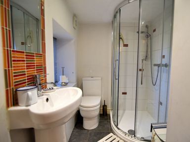 A bathroom with a sink, toilet, curved glass shower, and striped tiles at Little Bay View in Lyme Regis