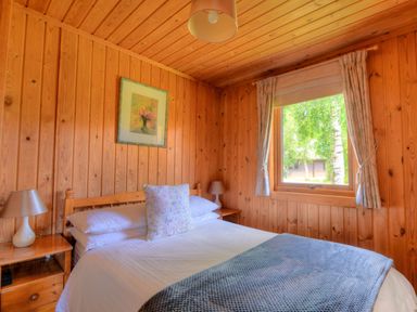 A bedroom with wooden walls and ceiling a bed with white sheets two bedside tables with lamps and a window with curtains at 4 Pinewood Retreat in Pinewood