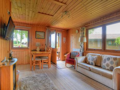 A wooden room with a sofa and armchair a dining table with chairs a wall-mounted TV and windows at 4 Pinewood Retreat in Pinewood