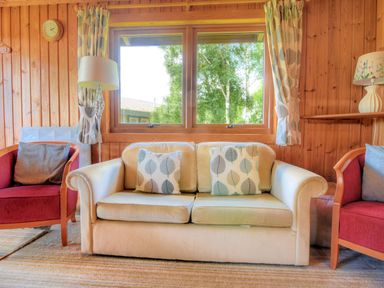 A sitting area with a beige sofa with patterned cushions two red armchairs and a window at 4 Pinewood Retreat in Pinewood