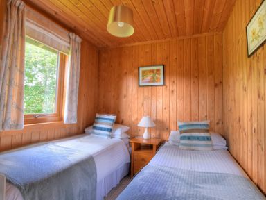 A bedroom with two single beds a nightstand with a lamp wooden walls and window at 4 Pinewood Retreat in Pinewood