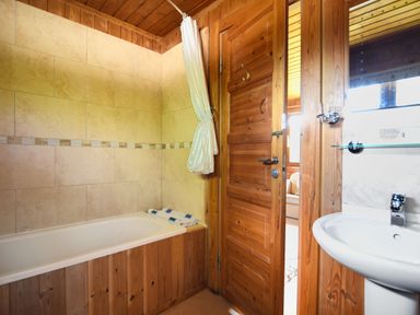 A bathroom with a bathtub tiled walls wooden door and a white sink at 4 Pinewood Retreat in Pinewood