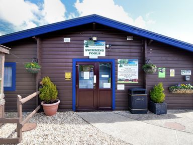 The entrance to a wooden building with a blue roof and signs for swimming pools at 4 Pinewood Retreat in Pinewood