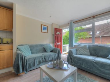A living room with two blue sofas a white coffee table and a red front door at 36 Fernhill Heights in Charmouth