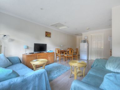 A living room with two blue sofas a wooden TV stand with a television and a dining table with chairs at 36 Fernhill Heights in Charmouth