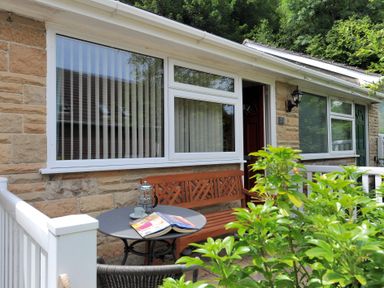 An outdoor seating area with a round table, bench, chair, and greenery at 36 Fernhill Heights Charmouth