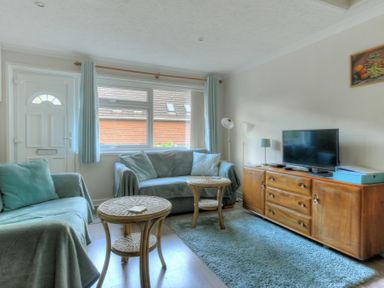 A living room with two sofas a wooden sideboard a flat screen tv and two round wicker tables at 36 Fernhill Heights in Charmouth