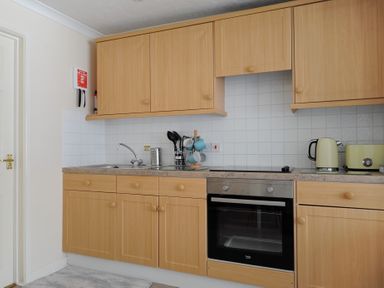 A kitchen with wooden cabinets a stainless steel oven a sink kitchen utensils mugs kettle and toaster at 36 Fernhill Heights in Charmouth