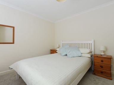 A bedroom with a white bed and wooden bedside tables with lamps at 36 Fernhill Heights in Charmouth
