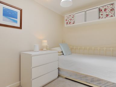 A bedroom with a single bed next to a white chest of drawers with a lamp and storage boxes above at 36 Fernhill Heights in Charmouth