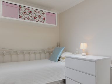 A small bedroom with a white metal bed a white dresser with a lamp and storage boxes above the bed at 36 Fernhill Heights in Charmouth