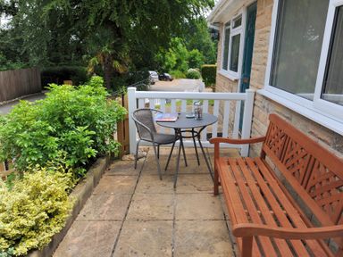 A small outdoor patio with a wooden bench metal chair and round table with a teapot and magazine at 36 Fernhill Heights in Charmouth
