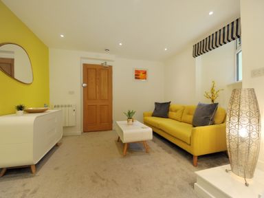 A living room with a yellow sofa a white coffee table a white sideboard and a wooden door at Seashore in Lyme Regis