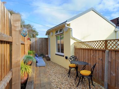 A narrow outdoor patio with wooden fencing a small table with two chairs and cushions and plants along a bench at Seashore in Lyme Regis