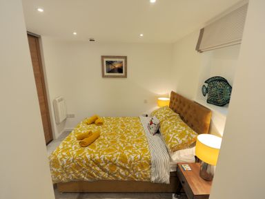 A bedroom with a bed with yellow floral bedding yellow lamps and a wooden nightstand at Seashore in Lyme Regis