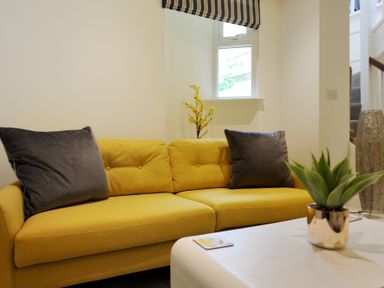 A yellow sofa with gray cushions near a window and a white table with a plant at Seashore in Lyme Regis