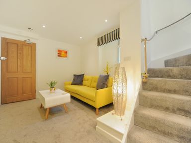A living room with a yellow sofa a white coffee table and carpeted stairs at Seashore in Lyme Regis