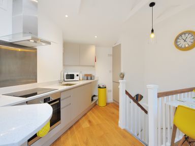 A kitchen with cabinets a stove a microwave a yellow trash bin and a staircase with a dining table and yellow chair at Seashore in Lyme Regis