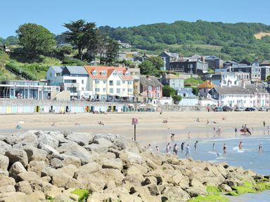A beach with people near the water and colorful houses along the shore at Seashore in Lyme Regis