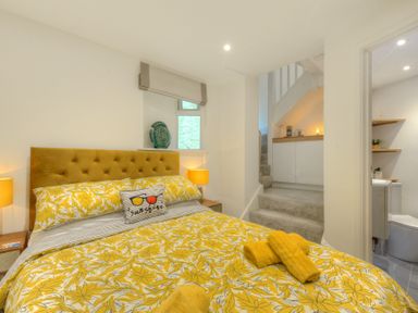 A bedroom with a yellow floral bedspread and pillow with stairs and a bathroom in the background at Seashore Lyme Regis