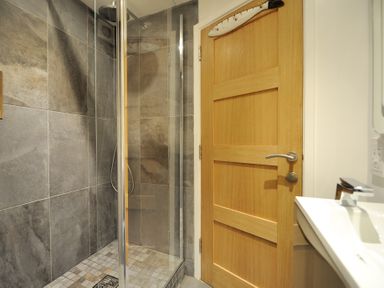 A bathroom with a glass shower enclosure and tiled walls next to a wooden door at Seashore Lyme Regis