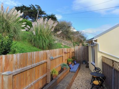 A narrow outdoor space with gravel ground a wooden fence plants and seating beside a yellow building at Seashore in Lyme Regis