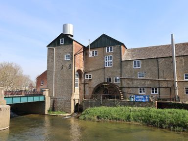 A building with a water wheel next to a river at The Dairy in Bridport
