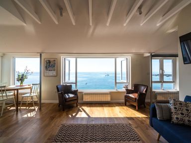 A living room with two leather armchairs a round wooden table with chairs and large windows showing a sea view at 3 Beach Way House Lyme Regis