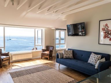 A living room with a blue sofa pillows two brown armchairs a rug and large windows overlooking the sea at 3 Beach Way House Lyme Regis