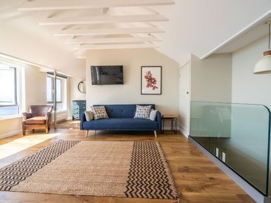 A sitting area with a blue sofa, leather armchair, wall-mounted tv, artwork, and wooden floor at 3 Beach Way House Lyme Regis