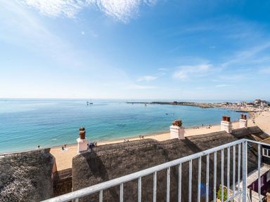 A balcony view of a beach with thatched roofs and the sea at 3 Beach Way House Lyme Regis