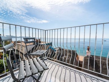 A balcony with metal chairs and railing overlooking rooftops and the sea at 3 Beach Way House in Lyme Regis
