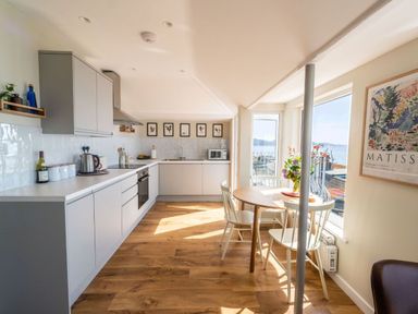 A kitchen with white cabinets wooden floor a round dining table with chairs and large windows at 3 Beach Way House Lyme Regis