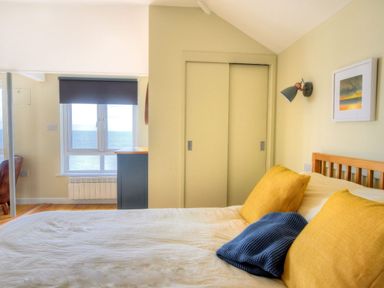 A bedroom with a bed with yellow pillows and a blue blanket and a window with a sea view at 3 Beach Way House Lyme Regis