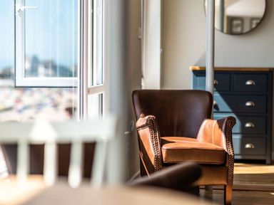 A room with a brown leather armchair near an open window and a blue chest of drawers with a round mirror above at 3 Beach Way House Lyme Regis