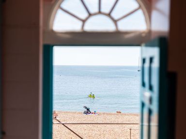 View through an open door to a beach with people and a kayak on the water at 3 Beach Way House in Lyme Regis