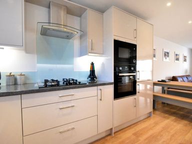 A modern kitchen with a stove gas cooktop hood oven microwave and pantry cabinets next to a dining table and bench seating at Shire View in Lyme Regis