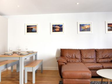 A living area with a brown leather sofa and a dining table with benches and plates on it at Shire View in Lyme Regis