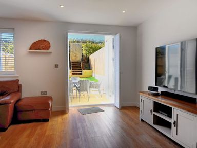 A living room with a brown sofa a television on a wooden cabinet and a table with chairs outside at Shire View Lyme Regis