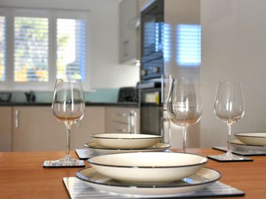 A dining table set with plates and wine glasses in a kitchen with cabinets and a window at Shire View in Lyme Regis