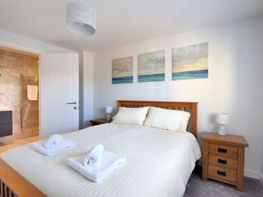 A bedroom with a double bed with white bedding and pillows bedside tables with lamps and a bathroom visible through an open door at Shire View in Lyme Regis