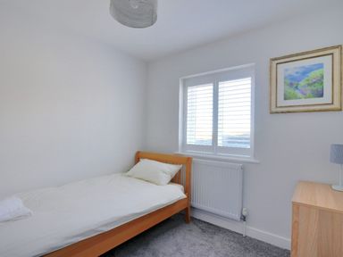 A bedroom with a single bed a wooden dresser a window with blinds and a framed picture on the wall at Shire View in Lyme Regis