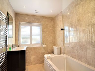 A bathroom with a bathtub a sink a toilet and a window with shutters at Shire View in Lyme Regis