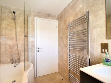 A bathroom with a bathtub shower combination a towel radiator and a sink at Shire View in Lyme Regis
